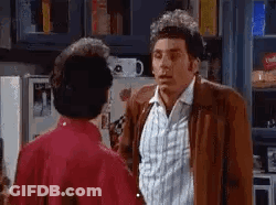 A Man In A Brown Jacket Is Talking To Another Man In A Red Shirt In A Kitchen . GIF