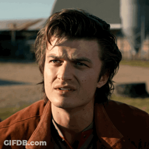 A Man In A Brown Jacket Looks At The Camera GIF