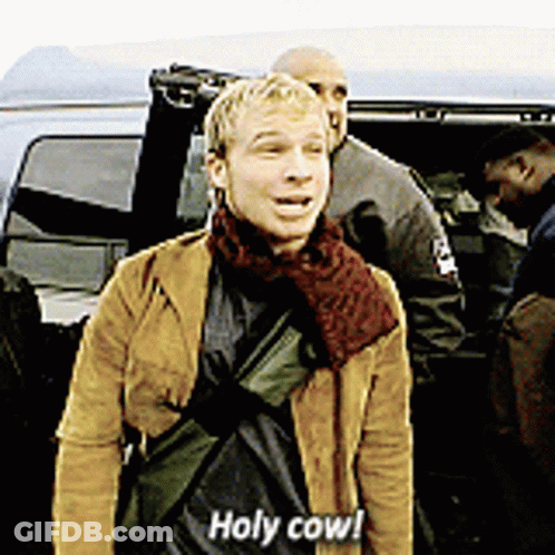 A Man In A Brown Jacket Says Holy Cow In Front Of A Car GIF