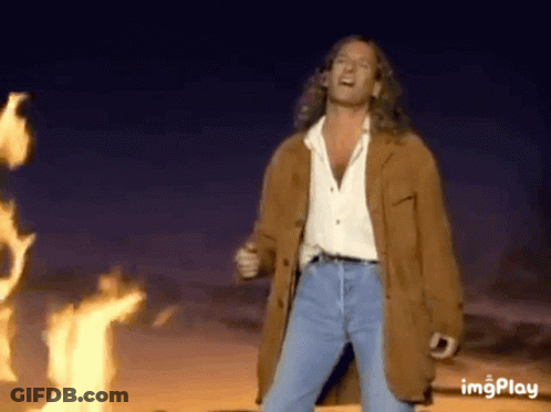 Man In Brown Jacket In Front Of Fire GIF