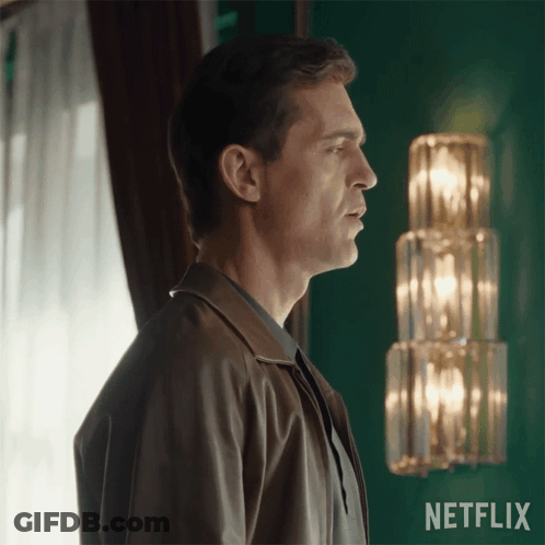 A Man In A Brown Jacket Stands In Front Of A Netflix Sign GIF