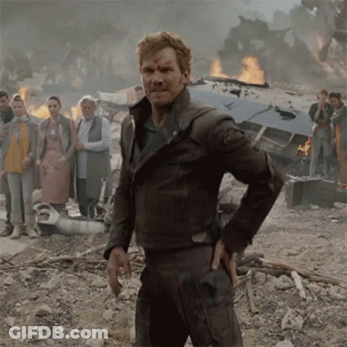 A Man In A Brown Leather Jacket Stands In Front Of A Burning Building GIF