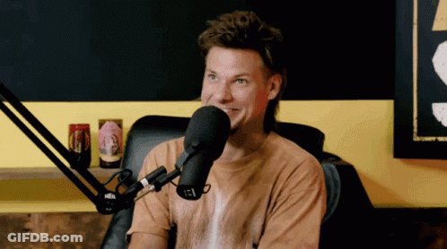 A Man In A Brown Shirt Is Sitting In Front Of A Microphone With A Sticker On It That Says Igl GIF