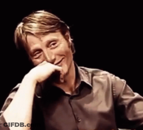 A Man In A Brown Shirt Is Smiling With His Hand On His Face . GIF