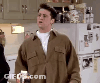 A Man In A Brown Shirt Is Standing In Front Of A Refrigerator Holding A Bottle Of Milk . GIF