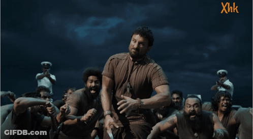 A Man In A Brown Shirt Stands In Front Of A Group Of People With Xhk Written On The Bottom GIF