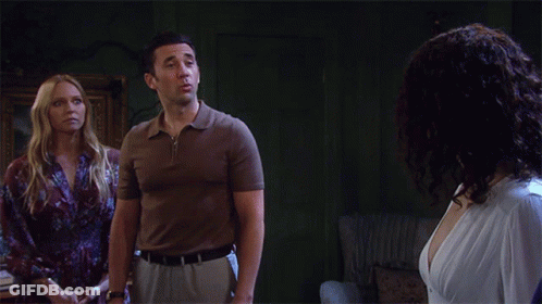 A Man In A Brown Shirt Stands Next To A Woman In A White Dress GIF