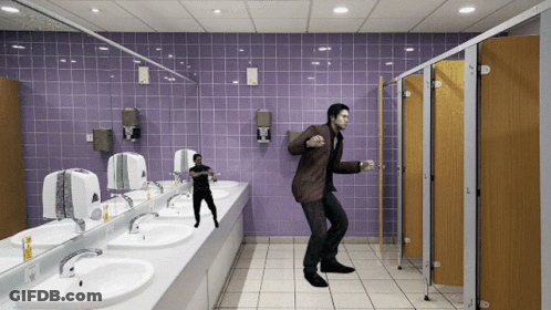 A Man In A Brown Suit Is Dancing In A Public Restroom GIF