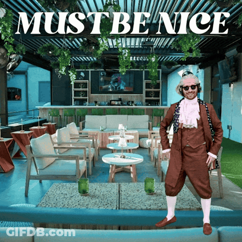 A Man In A Brown Suit Stands In Front Of A Restaurant With The Words Must Be Nice Above Him GIF