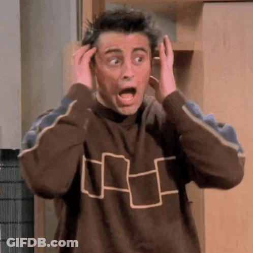 A Man In A Brown Sweater Is Making A Surprised Face While Holding His Hands To His Head . GIF