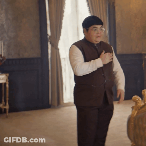 A Man In A Brown Vest And White Shirt Is Standing In A Room GIF