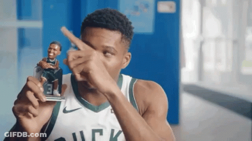 A Man In A Bucks Jersey Is Holding A Figurine Of A Basketball Player And Pointing At It . GIF