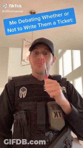 A Man In A Bullet Proof Vest Is Holding A Red Pen In His Mouth With A Tiktok Sticker Above Him GIF
