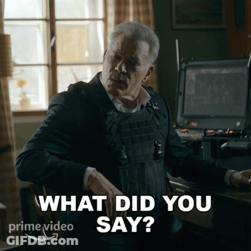 A Man In A Bullet Proof Vest Is Sitting At A Desk And Says What Did You Say GIF
