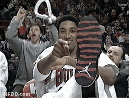 A Man In A Bulls Jersey Holds Up His Shoe In Front Of A Crowd GIF