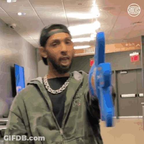 A Man In A Camo Jacket Holds A Blue Toy Gun In A Hallway GIF