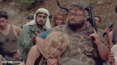 A Man In A Camo Shirt Holds A Gun While Holding A Woman GIF