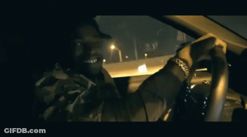A Man In A Camo Shirt Is Driving A Car At Night GIF