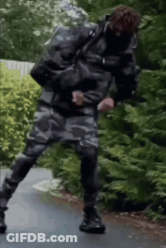 A Man In A Camouflage Jacket And Pants Is Standing On One Leg On A Road . GIF