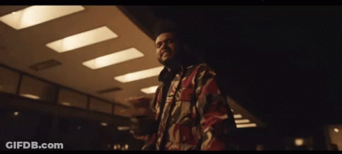 A Man In A Camouflage Jacket Is Standing In A Dark Room With A Ceiling Light . GIF