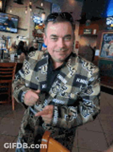A Man In A Camouflage Jacket Is Standing In A Restaurant . GIF