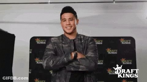 A Man In A Camouflage Jacket Is Standing With His Arms Crossed In Front Of A Draft Kings Sign . GIF