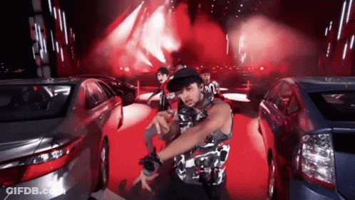 A Man In A Camouflage Shirt Is Dancing In Front Of A Crowd Of Cars GIF