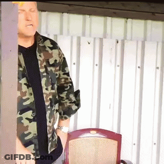 A Man In A Camouflage Shirt Is Standing In Front Of A Chair GIF