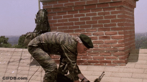 A Man In A Camouflage Uniform Is Working On A Brick Chimney GIF