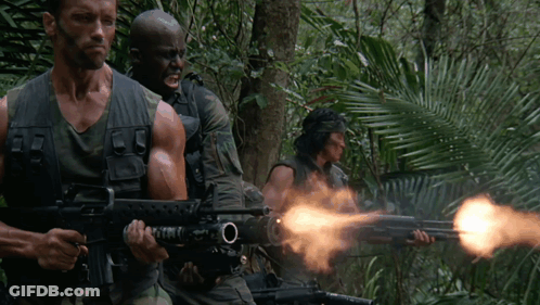 A Man In A Camouflage Vest Is Holding A Gun With The Letter O On The Barrel GIF