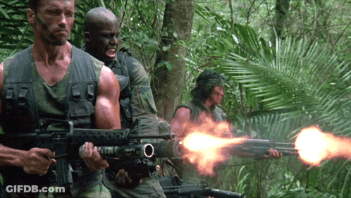 A Man In A Camouflage Vest Is Holding A Rifle With The Letter O On The Barrel GIF