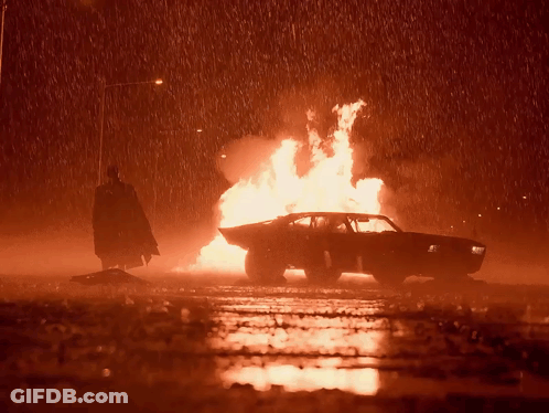A Man In A Cape Is Standing Next To A Burning Car GIF