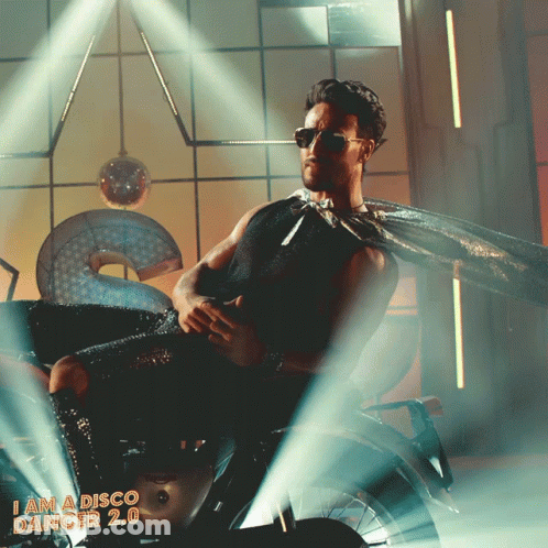 A Man In A Cape Sits On A Motorcycle With The Words I Am A Disco Dancer 2.0 On The Bottom GIF