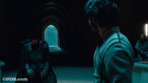A Man In A Cape Stands In Front Of A Man With A Headless Figure GIF