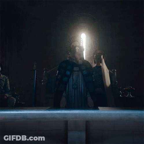 A Man In A Cape Stands In Front Of A Window With A Light Shining Through It GIF
