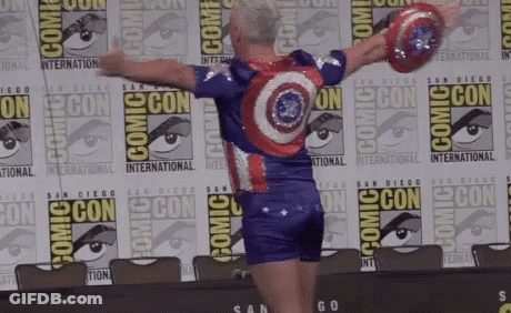 A Man In A Captain America Costume Is Standing In Front Of A Comic Con Sign GIF