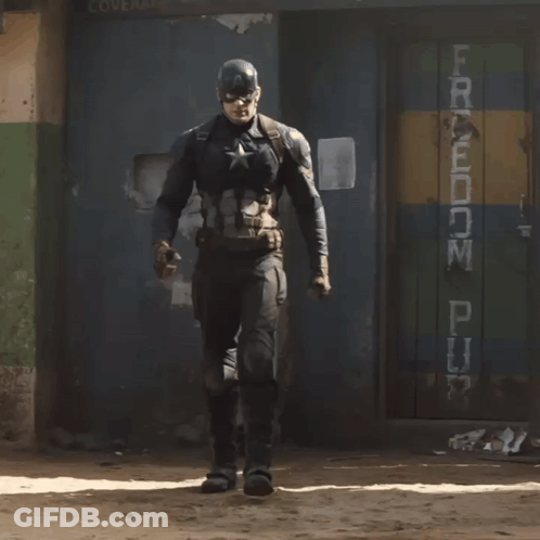 A Man In A Captain America Costume Stands In Front Of A Sign That Says Freedom GIF