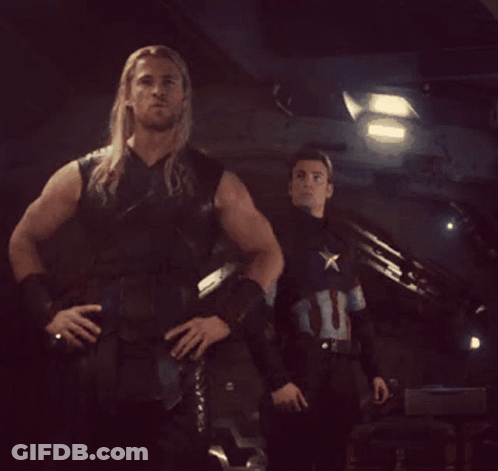 A Man In A Captain America Uniform Stands Next To A Man In A Leather Vest GIF