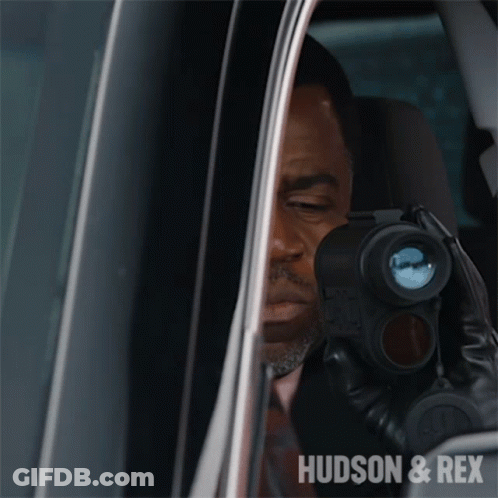 A Man In A Car Looking Through A Binoculars With The Words Hudson & Rex On The Bottom Right GIF