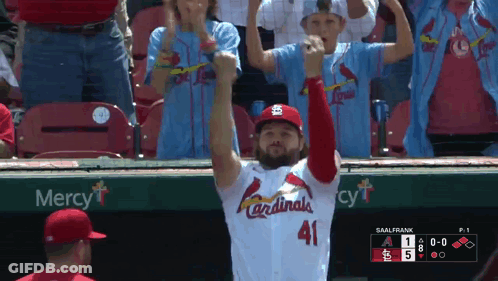 A Man In A Cardinals Jersey Stands In Front Of A Mercy Sign GIF