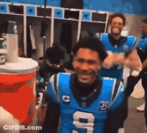 A Man In A Carolina Panthers Jersey Is Standing In A Locker Room . GIF