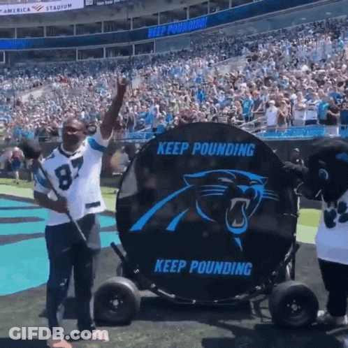A Man In A Carolina Panthers Jersey Is Standing In Front Of A Large Keep Pounding Sign GIF