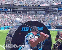 A Man In A Carolina Panthers Jersey Is Swinging A Bat At A Drum That Says Keep Fighting GIF