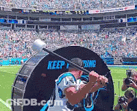 A Man In A Carolina Panthers Jersey Is Swinging A Bat In Front Of A Keep Fighting Sign GIF