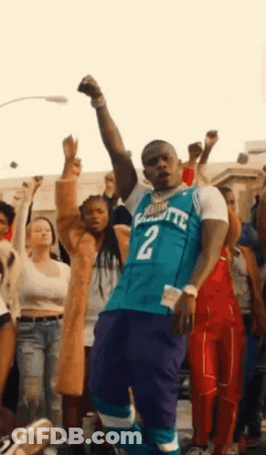 A Man In A Charlotte Hornets Jersey Is Standing In Front Of A Crowd Of People . GIF
