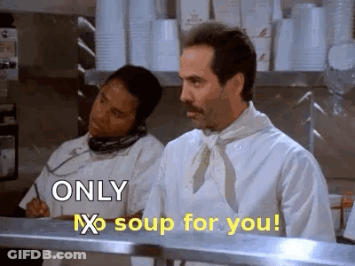 A Man In A Chef 'S Apron Is Standing In A Kitchen Talking On A Phone . GIF