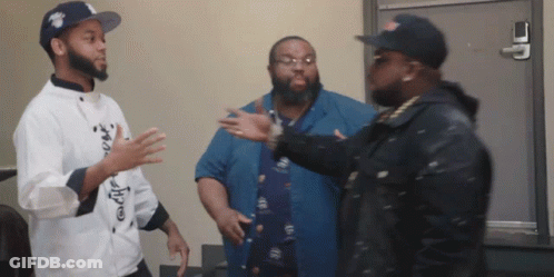 A Man In A Chef 'S Coat Talks To Two Other Men In A Room GIF