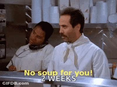 A Man In A Chef 'S Uniform Is Standing In A Kitchen Talking On A Cell Phone . GIF