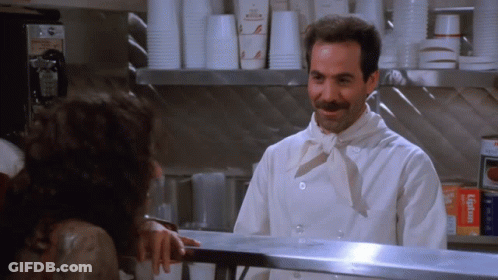 A Man In A Chef 'S Uniform Is Talking To A Woman Behind A Counter GIF