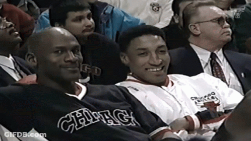 A Man In A Chicago Bulls Jersey Sits Next To Another Man GIF